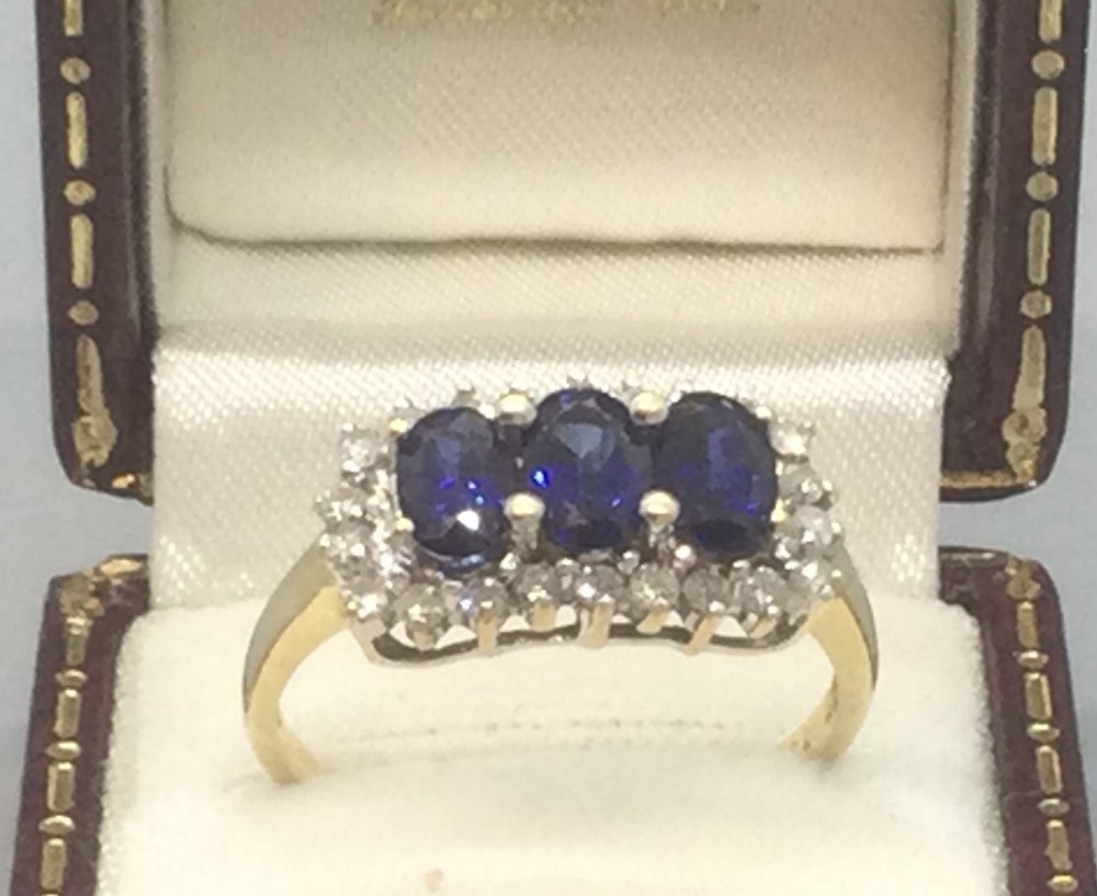 A 1960s 18ct yellow gold ring featuring three oval blue sapphires set horizontally within a rectangular border of round diamonds.