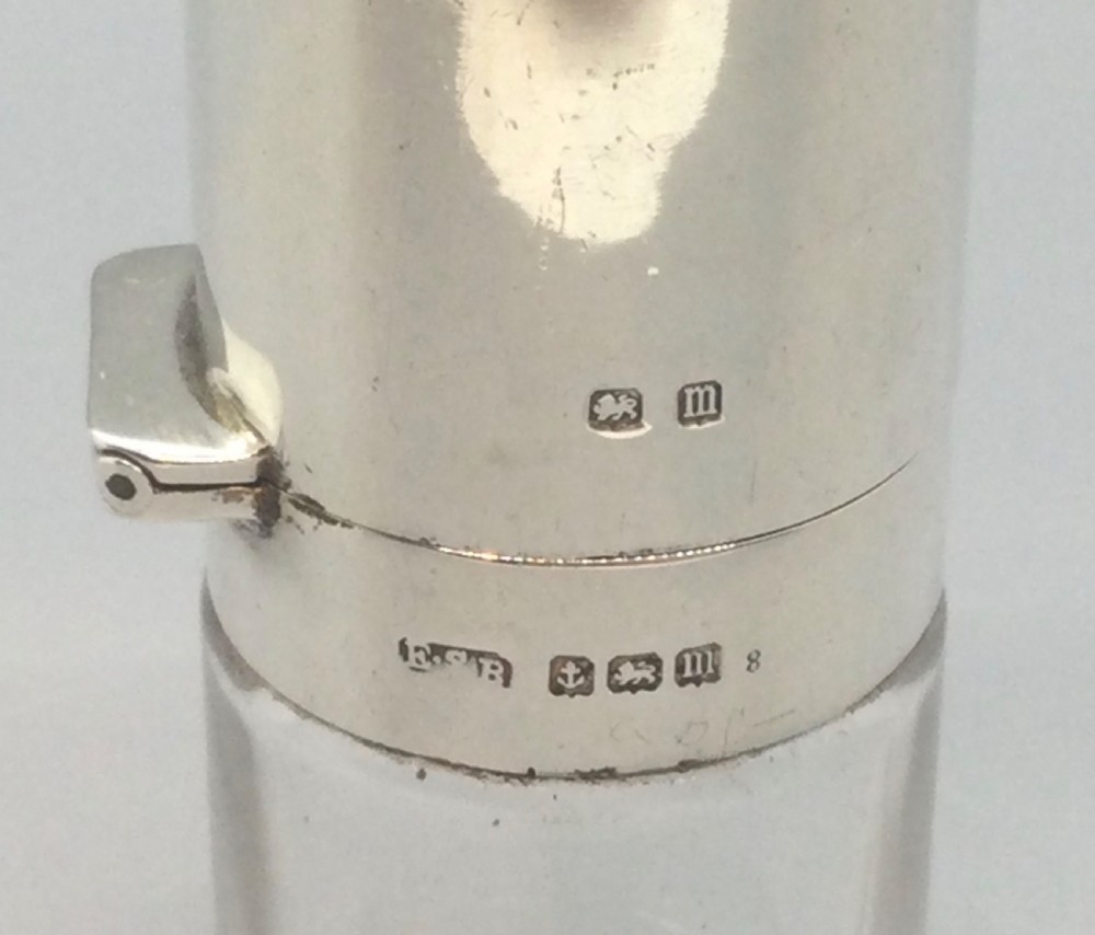 A cylindrical clear glass scent bottle with a sterling silver cap featuring an inlaid black enamel top decorated with a silver bow and garland motif. View V
