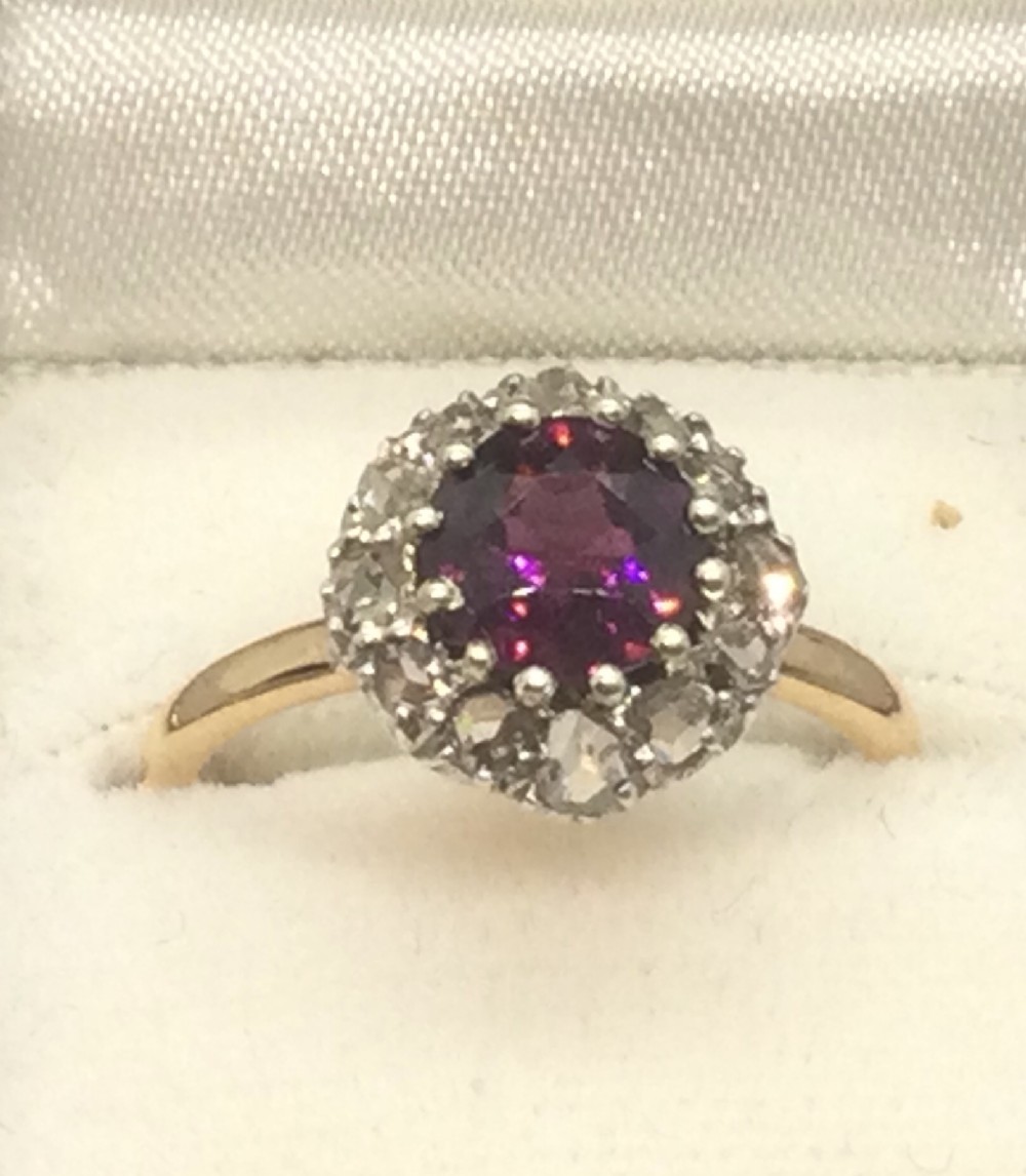 A vintage yellow gold ring featuring a central round purple-red ruby surrounded by a halo of small diamonds.
