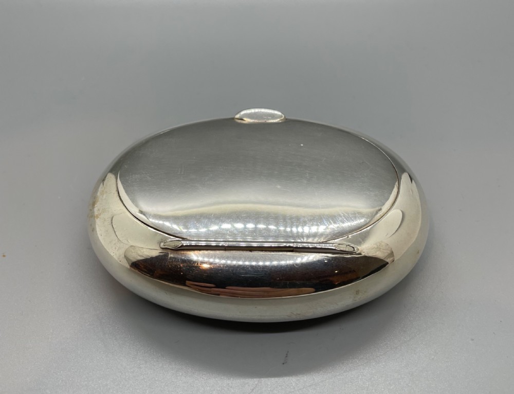 A smooth, oval sterling silver tobacco box with a polished finish and a hinged lid. View III