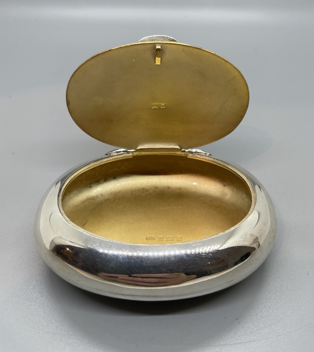 A smooth, oval sterling silver tobacco box with a polished finish and a hinged lid. View VI