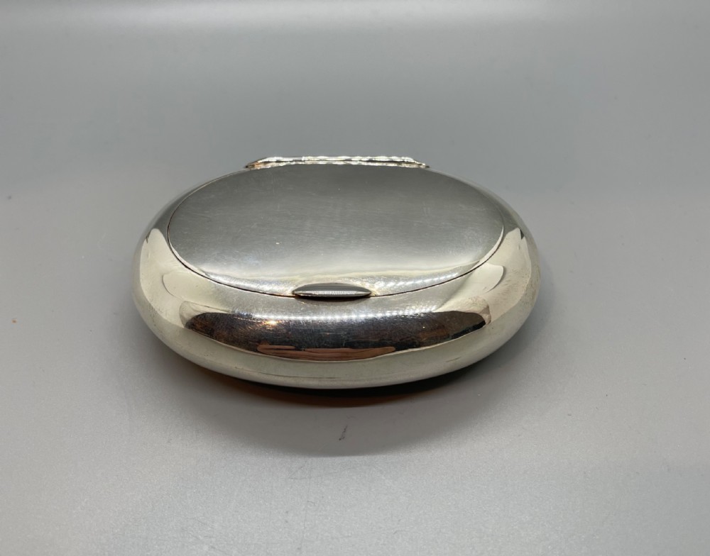 A smooth, oval sterling silver tobacco box with a polished finish and a hinged lid. View IX