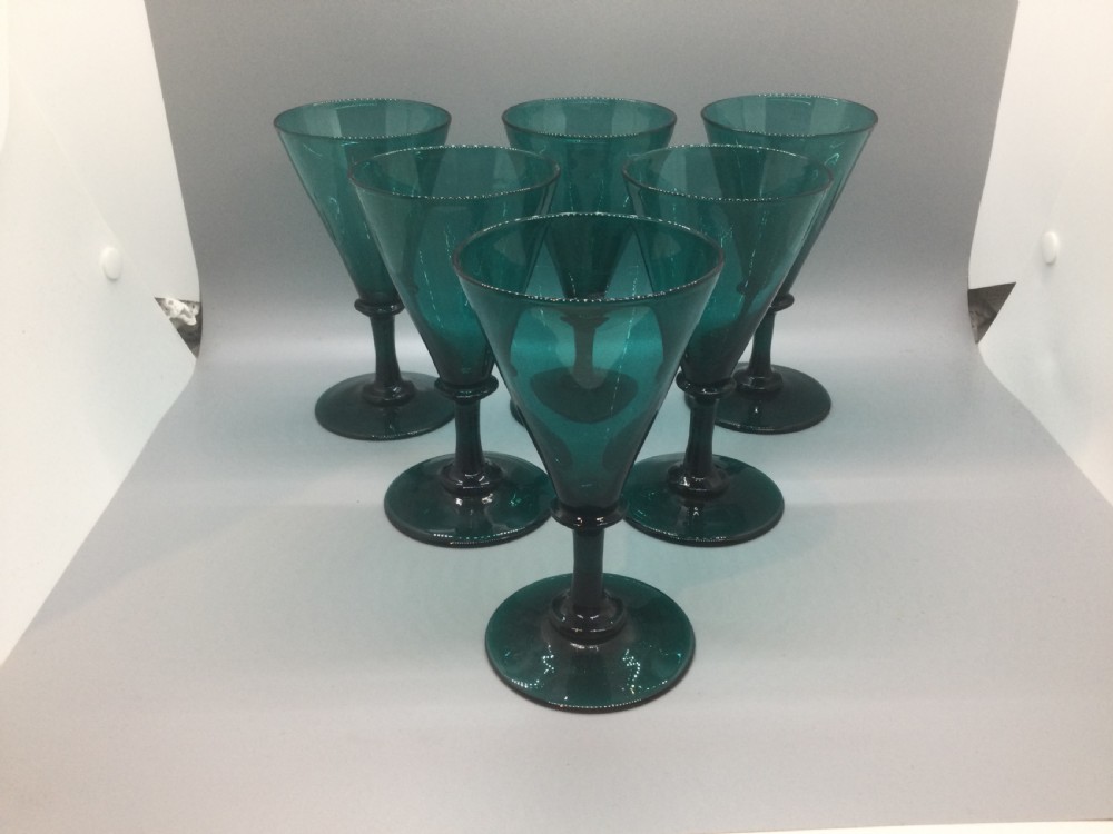 A set of six dark green hand-blown Georgian wine glasses arranged on a neutral grey background.