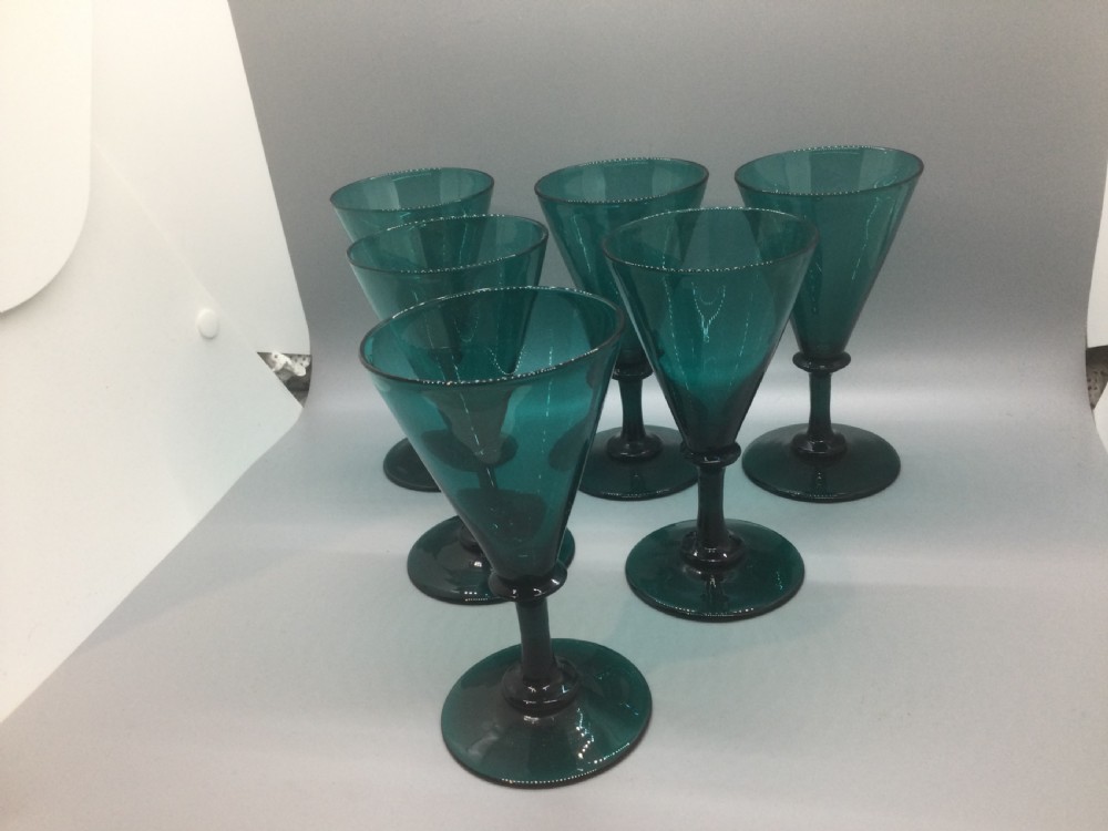 A set of six dark green hand-blown Georgian wine glasses arranged on a neutral grey background. View II