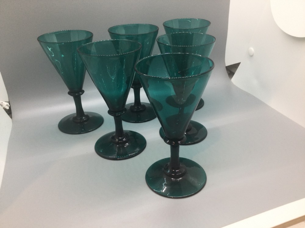 A set of six dark green hand-blown Georgian wine glasses arranged on a neutral grey background. View III