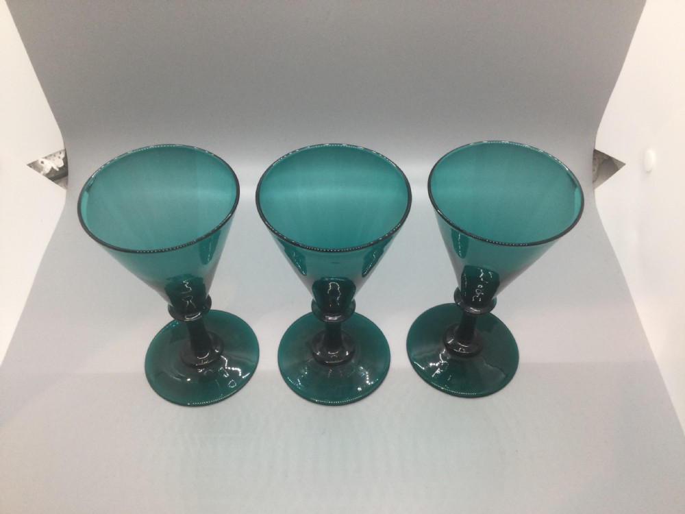 A set of six dark green hand-blown Georgian wine glasses arranged on a neutral grey background. View IV