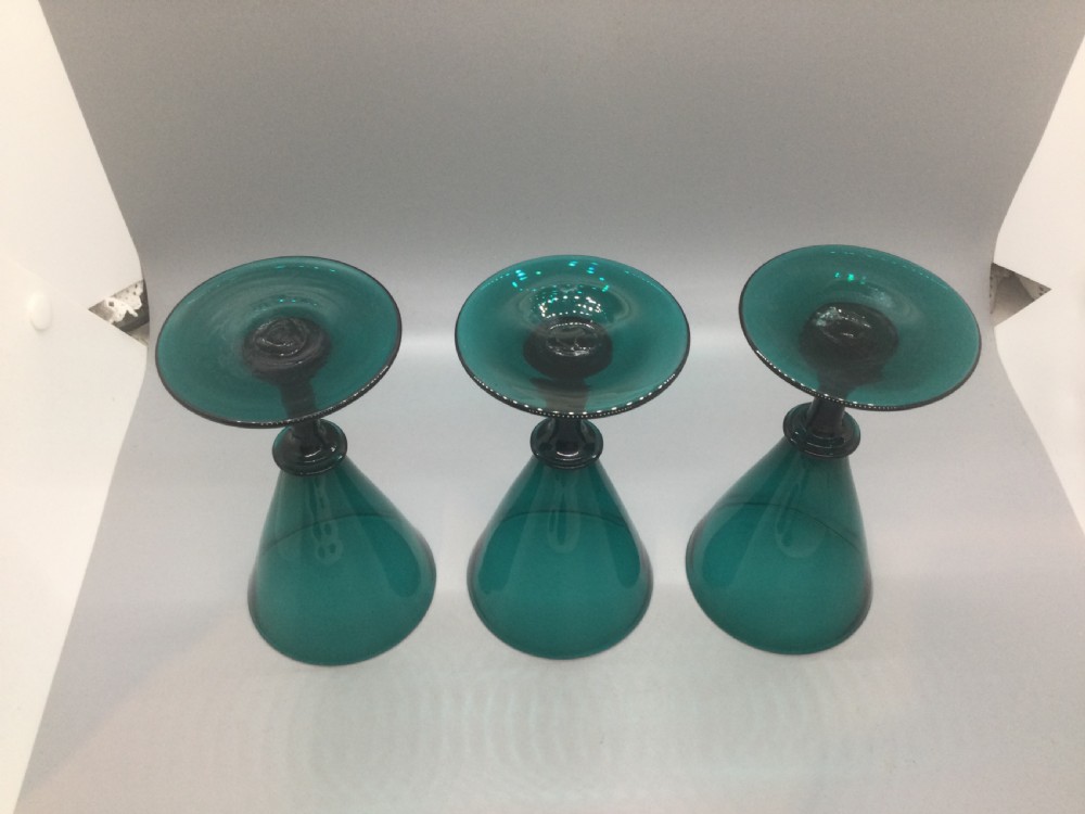 A set of six dark green hand-blown Georgian wine glasses arranged on a neutral grey background. View V