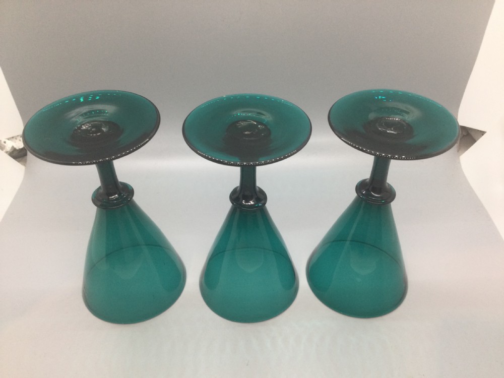 A set of six dark green hand-blown Georgian wine glasses arranged on a neutral grey background. View VI