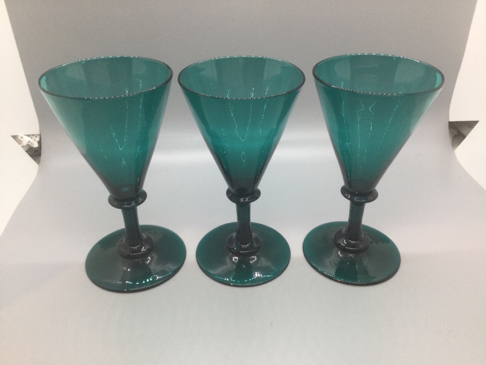 A set of six dark green hand-blown Georgian wine glasses arranged on a neutral grey background. View VII