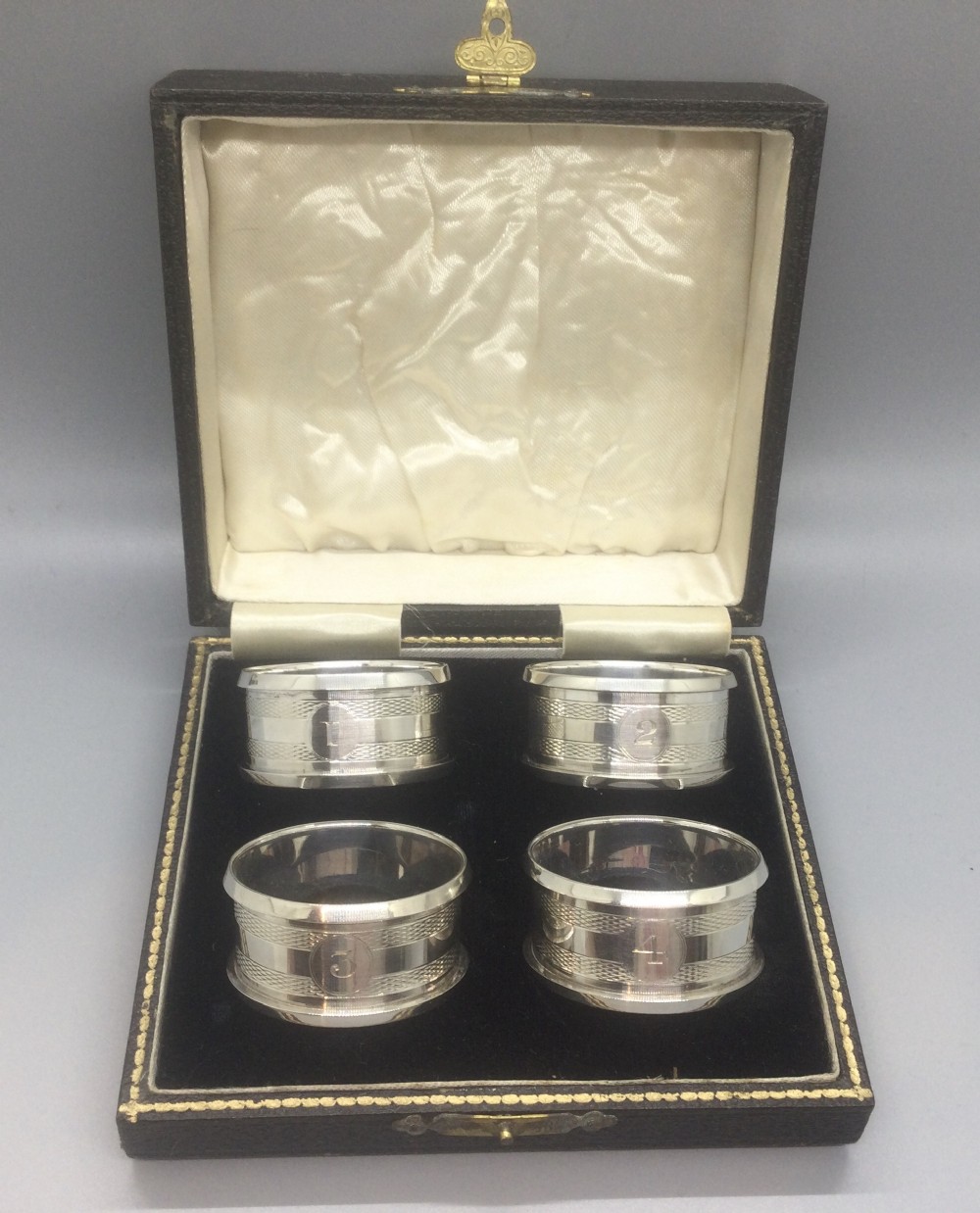 A set of four numbered sterling silver napkin rings featuring engine-turned decoration, presented in an open fitted leatherette box.