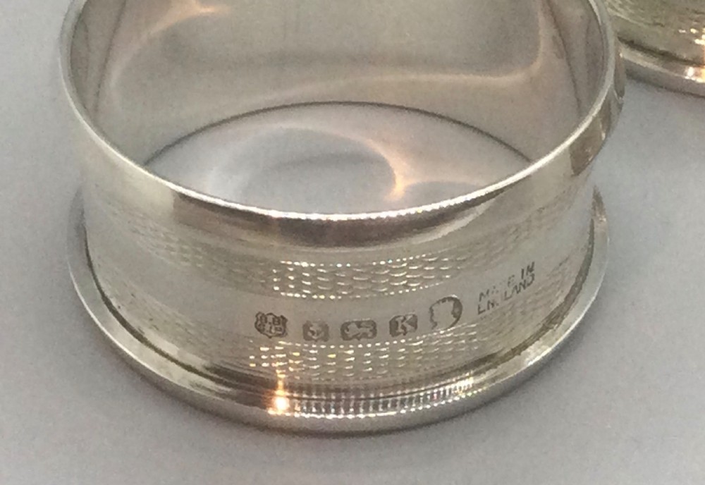 A set of four numbered sterling silver napkin rings featuring engine-turned decoration, presented in an open fitted leatherette box. View IV
