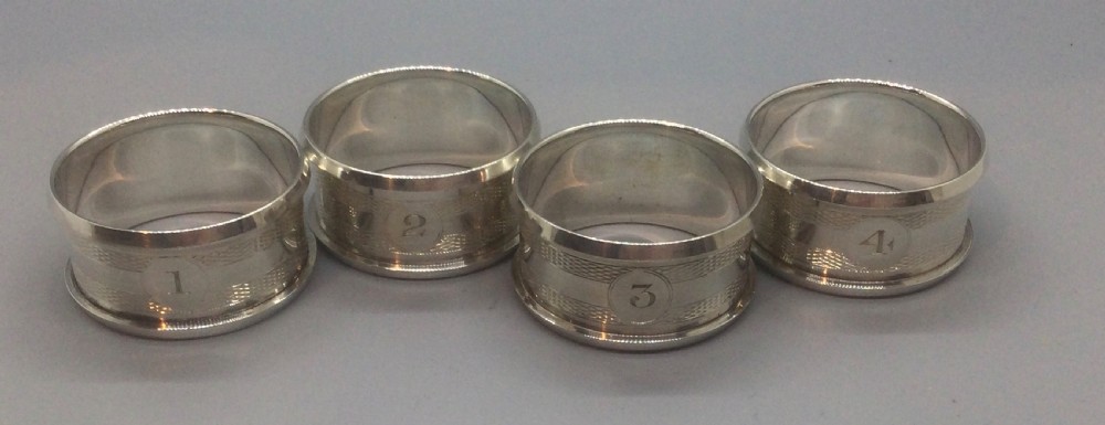 A set of four numbered sterling silver napkin rings featuring engine-turned decoration, presented in an open fitted leatherette box. View VI