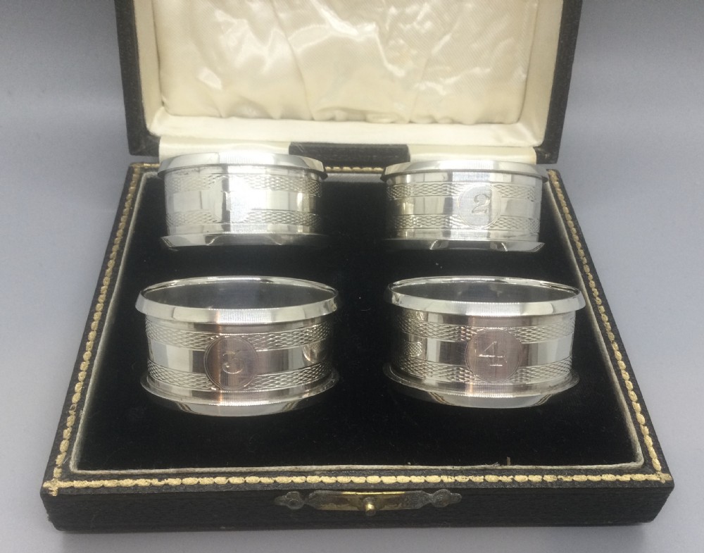 A set of four numbered sterling silver napkin rings featuring engine-turned decoration, presented in an open fitted leatherette box. View VIII