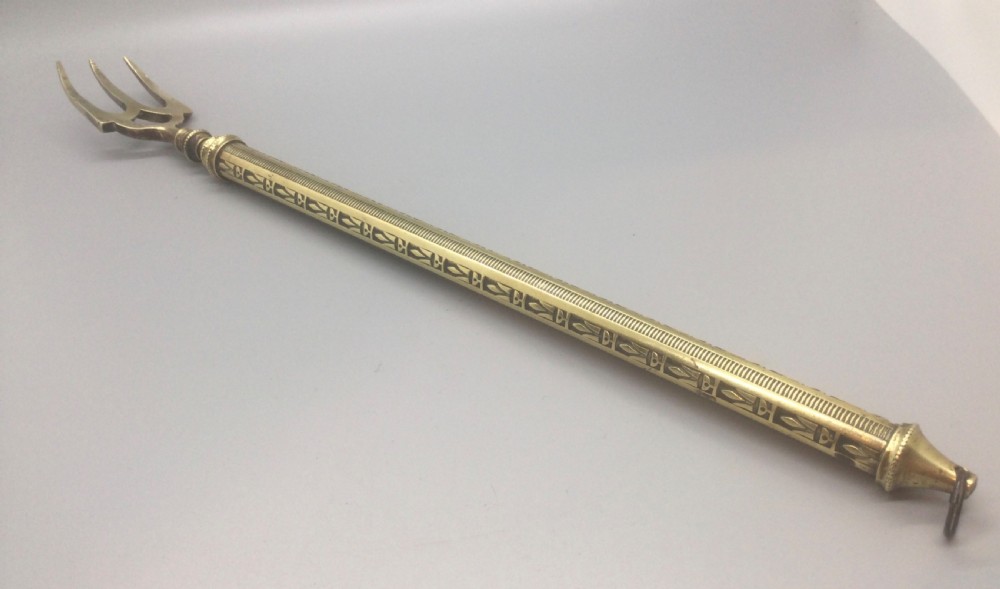 An antique Victorian extendable brass toasting fork with three prongs, an engraved geometric handle, and a hanging loop. View II