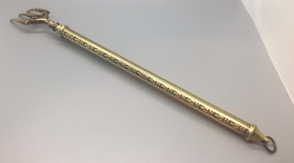 An antique Victorian extendable brass toasting fork with three prongs, an engraved geometric handle, and a hanging loop. View IV