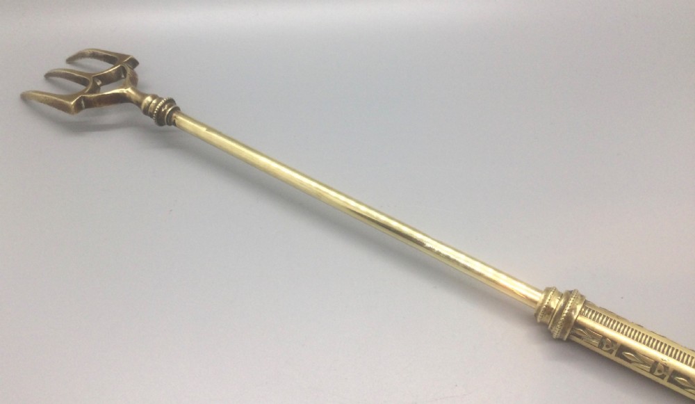 An antique Victorian extendable brass toasting fork with three prongs, an engraved geometric handle, and a hanging loop. View VI