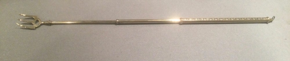 An antique Victorian extendable brass toasting fork with three prongs, an engraved geometric handle, and a hanging loop. View VII