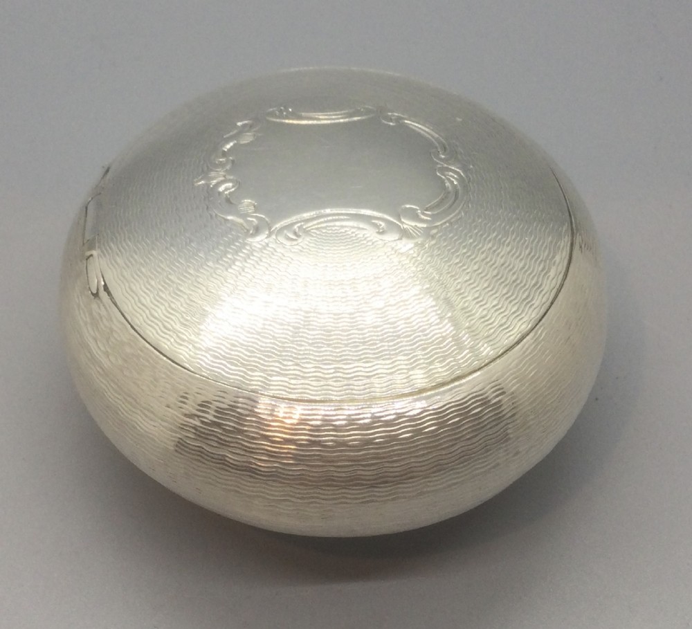 An oval Victorian sterling silver snuff box with engine-turned geometric engraving and a central vacant cartouche on top. View V