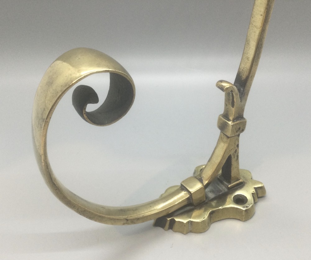 A Victorian solid brass coat and hat hook featuring scrolled upper and lower arms mounted on a shaped backplate. View V