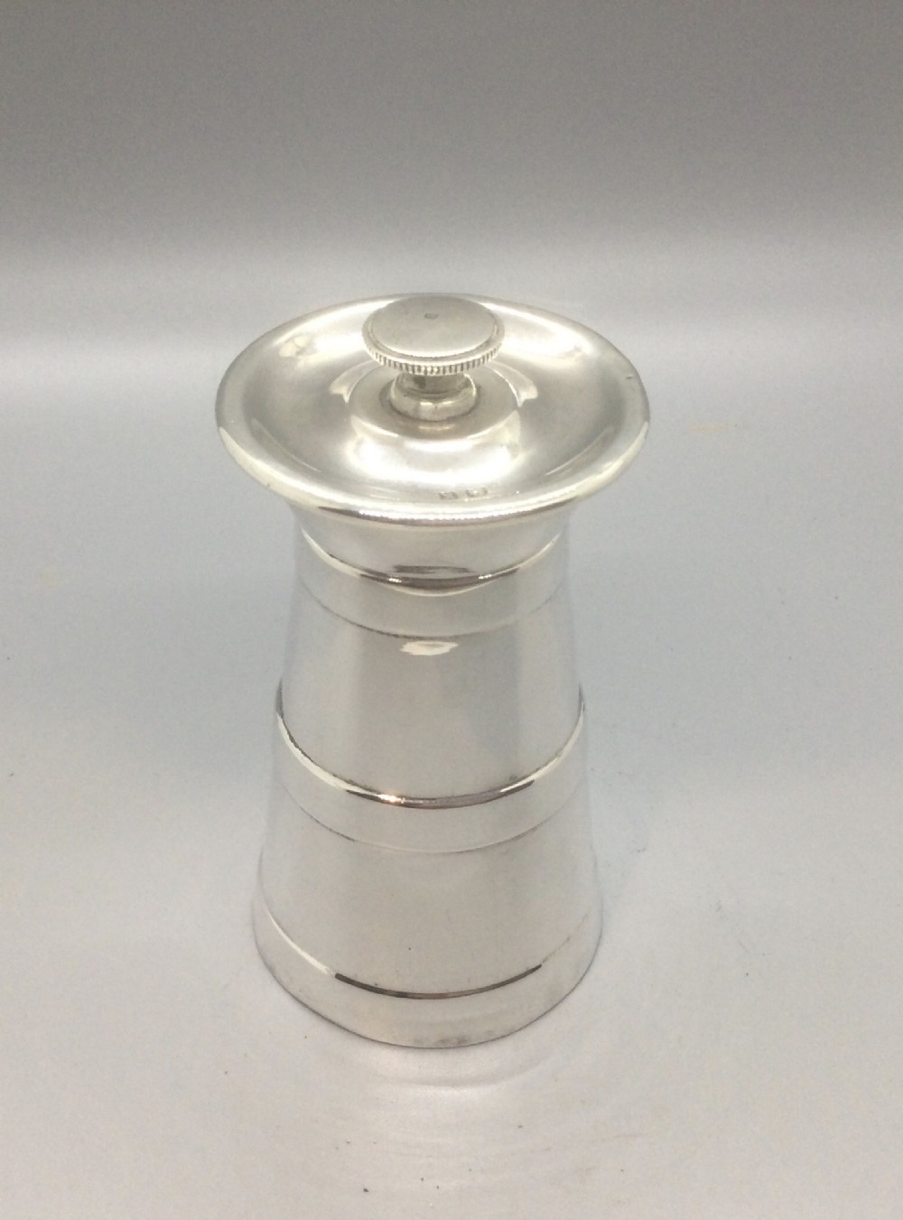 A tapered sterling silver pepper grinder with a flared top rim and knurled finial cap.