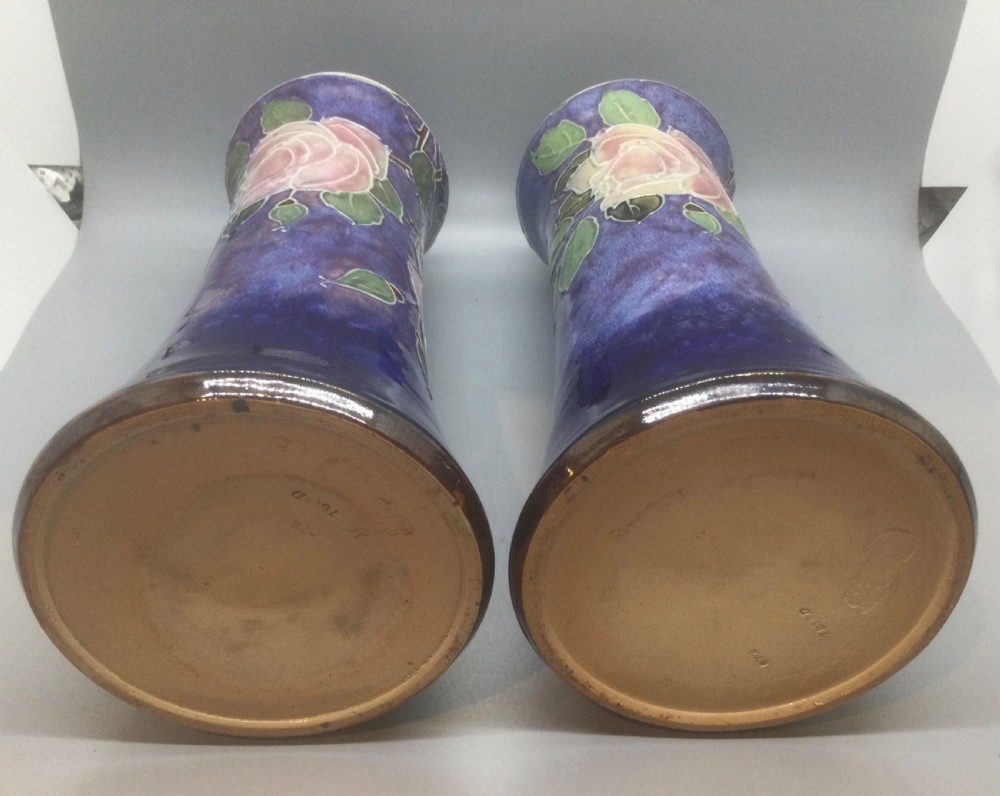 A matching pair of Royal Doulton Art Nouveau stoneware vases featuring stylized cream and soft pink rose motifs against a mottled cobalt blue background. View V