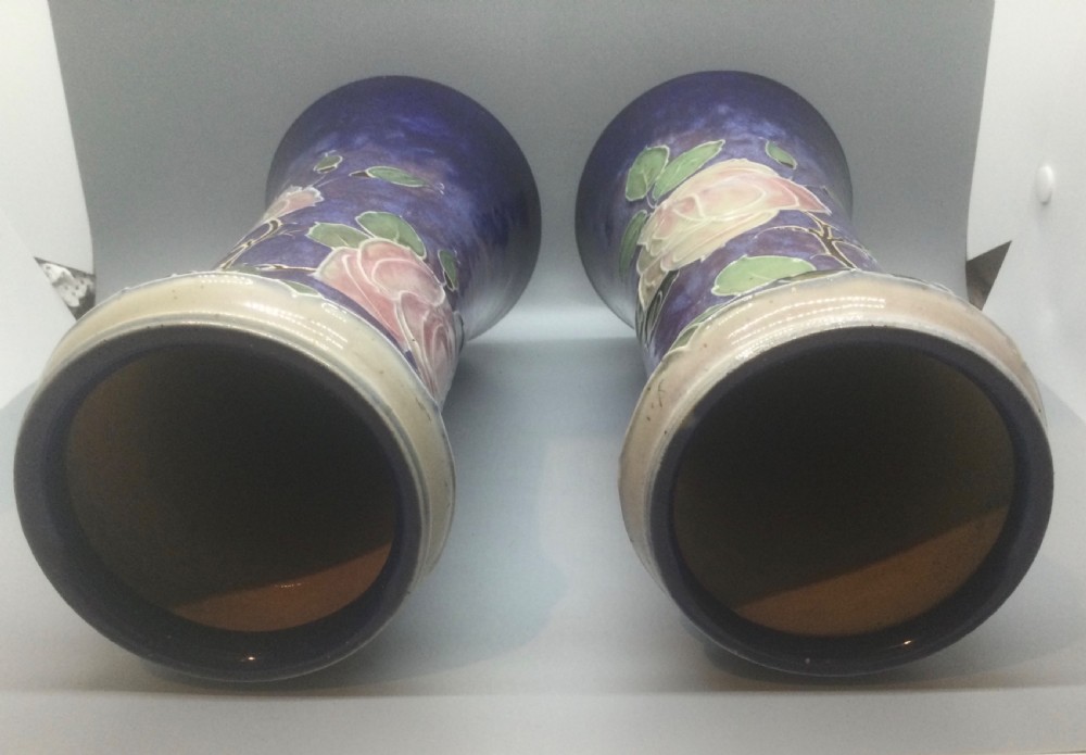 A matching pair of Royal Doulton Art Nouveau stoneware vases featuring stylized cream and soft pink rose motifs against a mottled cobalt blue background. View VI