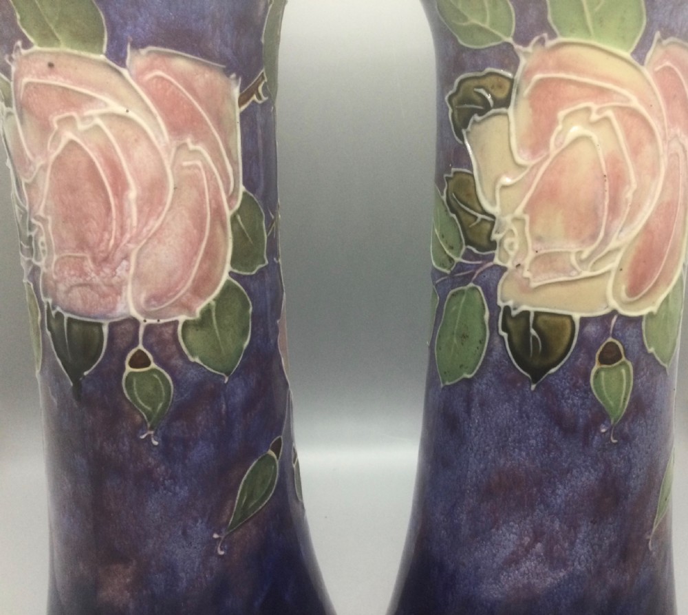 A matching pair of Royal Doulton Art Nouveau stoneware vases featuring stylized cream and soft pink rose motifs against a mottled cobalt blue background. View X