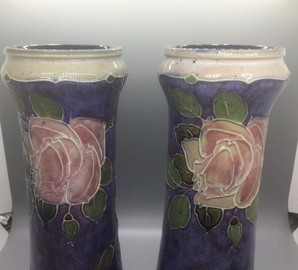 A matching pair of Royal Doulton Art Nouveau stoneware vases featuring stylized cream and soft pink rose motifs against a mottled cobalt blue background. View XI