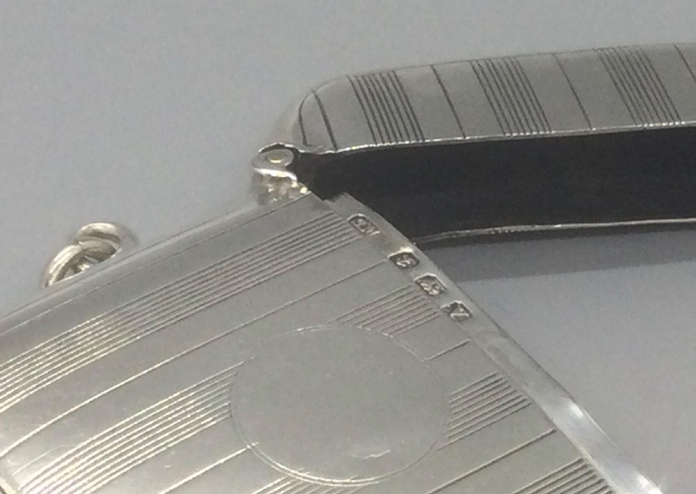 A square sterling silver Art Deco vesta case featuring engine-turned vertical line detailing, a circular central cartouche, a hinged top lid, and a suspension loop on the side. View VIII