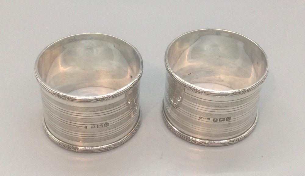 A pair of engine-turned sterling silver napkin rings with vacant oval cartouches, presented inside a blue velvet-lined fitted display case. View IV