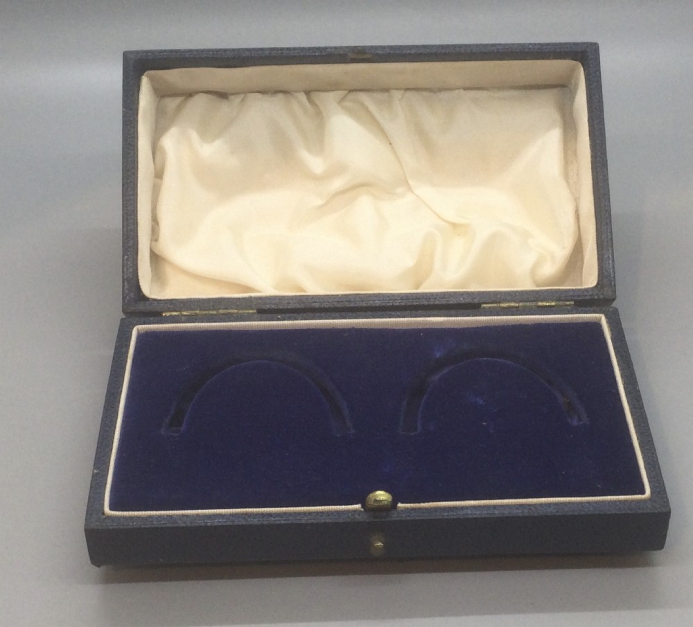 A pair of engine-turned sterling silver napkin rings with vacant oval cartouches, presented inside a blue velvet-lined fitted display case. View VI