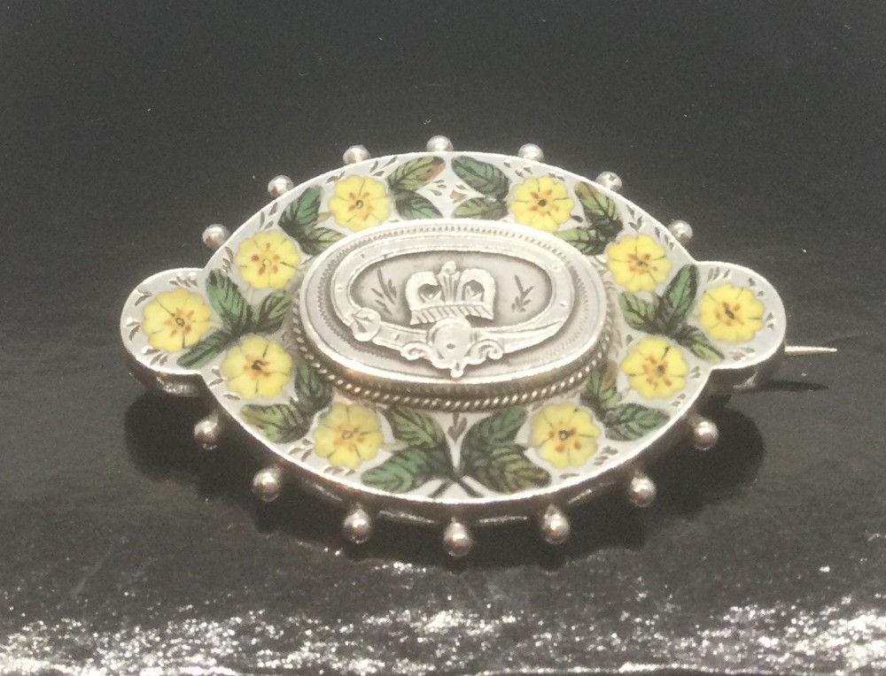 An oval Victorian silver brooch decorated with hand-painted yellow enamel flowers, green leaves, beaded outer edges, and a central silver crest motif.