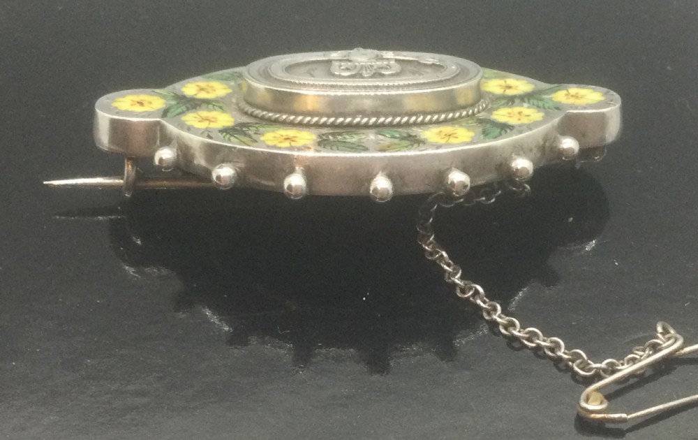 An oval Victorian silver brooch decorated with hand-painted yellow enamel flowers, green leaves, beaded outer edges, and a central silver crest motif. View VI