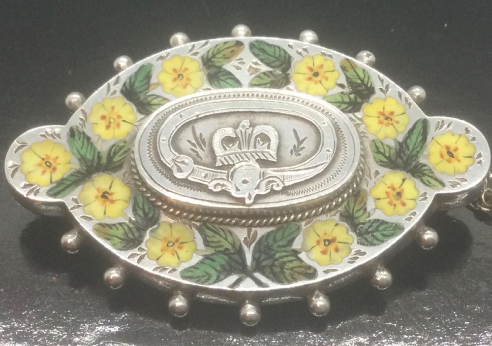 An oval Victorian silver brooch decorated with hand-painted yellow enamel flowers, green leaves, beaded outer edges, and a central silver crest motif. View VII