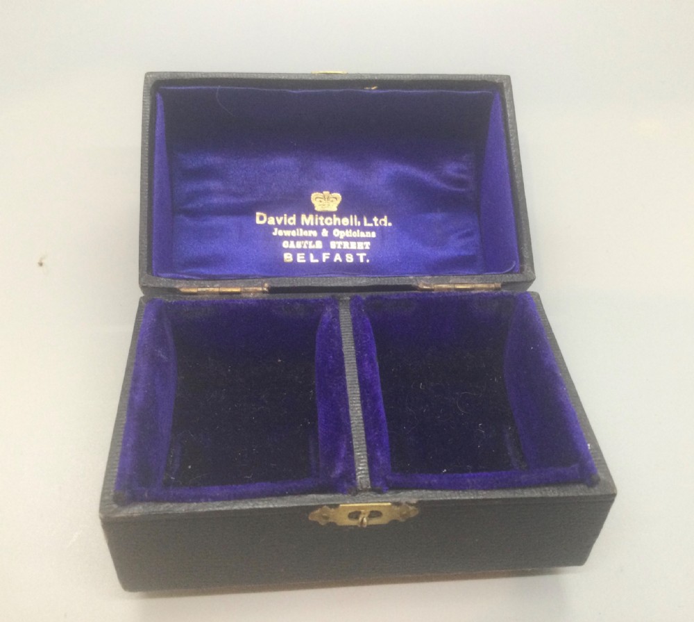 A pair of engine-turned sterling silver napkin rings with blank circular cartouches, displayed inside a black box with blue velvet and silk lining. View VIII