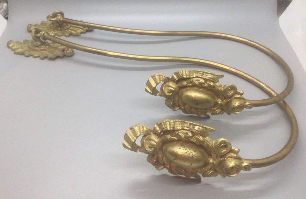 A pair of 19th-century French ormolu curtain tiebacks with long curved arms and ornamental floral backplates.