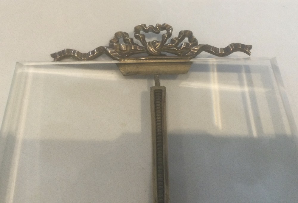 A late 19th-century French easel photo frame featuring thick bevelled glass, a ribbon bow top motif, spherical feet, and a gilded bronze framework. View VIII