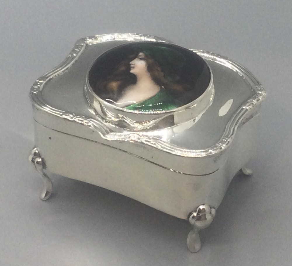 An Edwardian silver trinket box featuring a shaped rectangular body on four feet with a central circular hand-painted enamel plaque depicting a woman in profile wearing green. View II