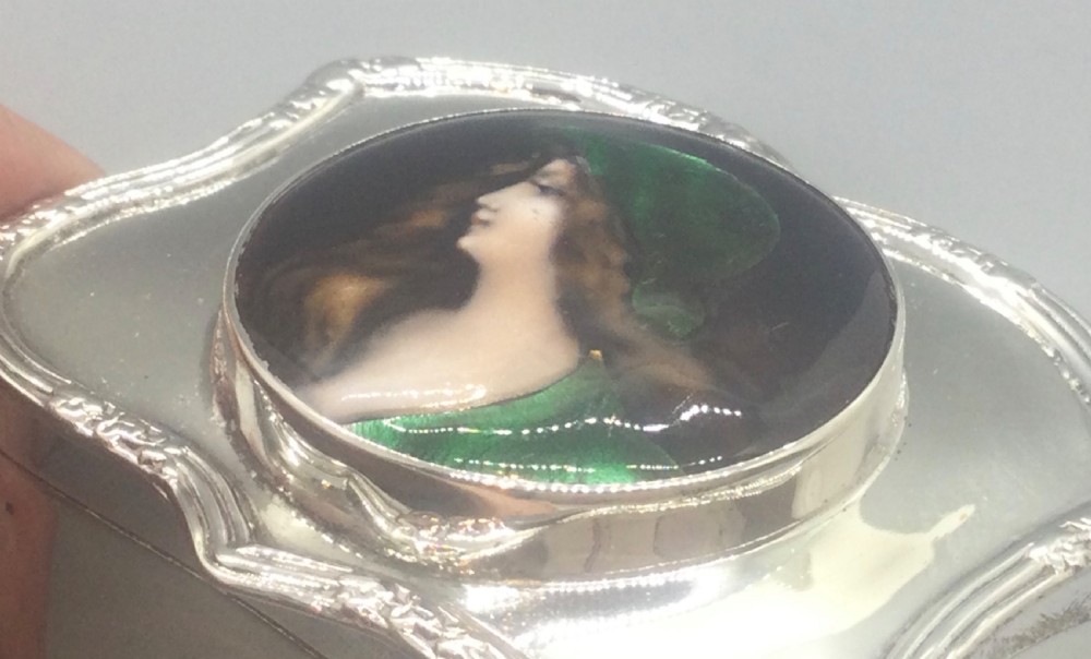An Edwardian silver trinket box featuring a shaped rectangular body on four feet with a central circular hand-painted enamel plaque depicting a woman in profile wearing green. View X