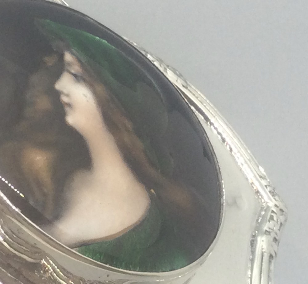 An Edwardian silver trinket box featuring a shaped rectangular body on four feet with a central circular hand-painted enamel plaque depicting a woman in profile wearing green. View XII
