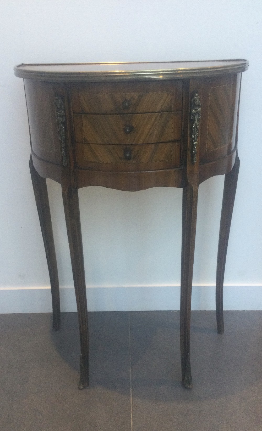 A late 19th-century French kingwood demi-lune console table featuring three drawers with geometric parquetry veneer, brass mounts, and long cabriole legs.