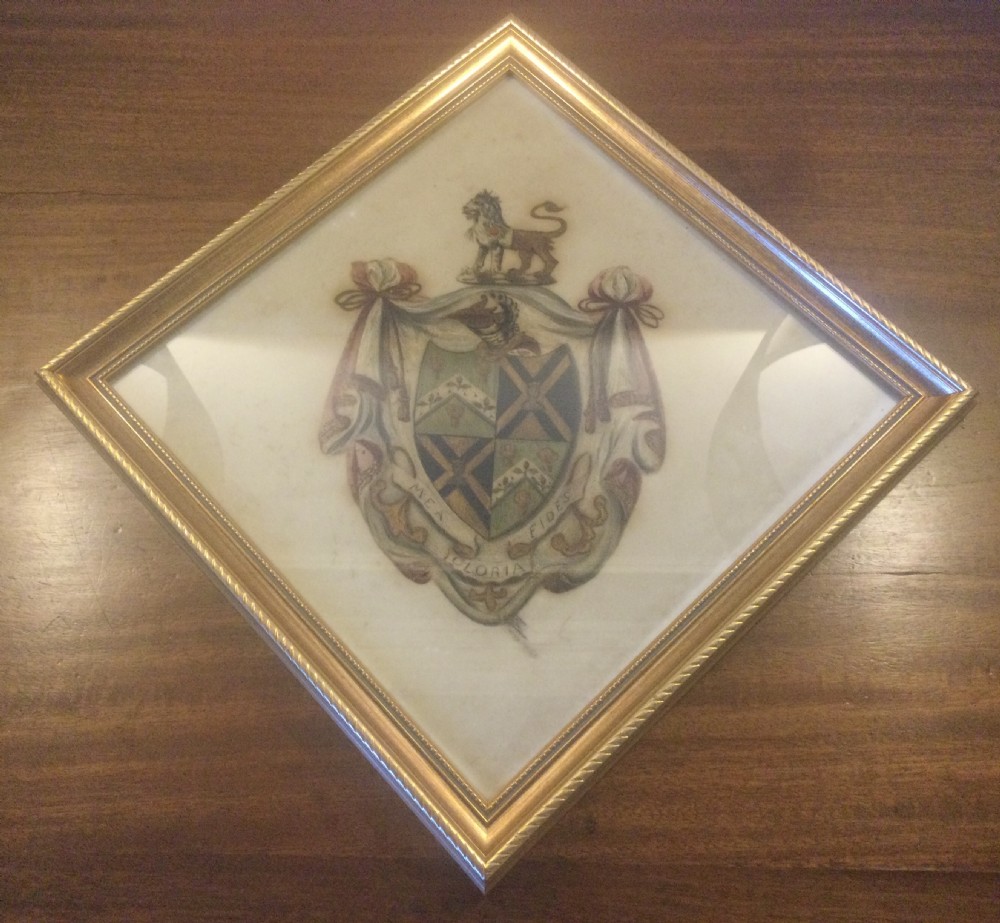 A diamond-shaped gilded frame housing a 19th-century oil painting on glass of an armorial crest with a lion, shield, and Latin motto banner.
