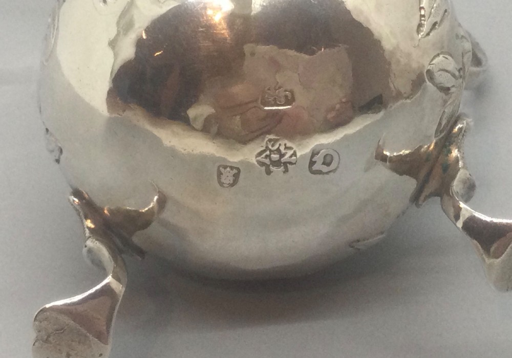 A George II sterling silver cream jug with hand-chased floral repousse decoration, a scalloped rim, scroll handle, and three pad feet. View V