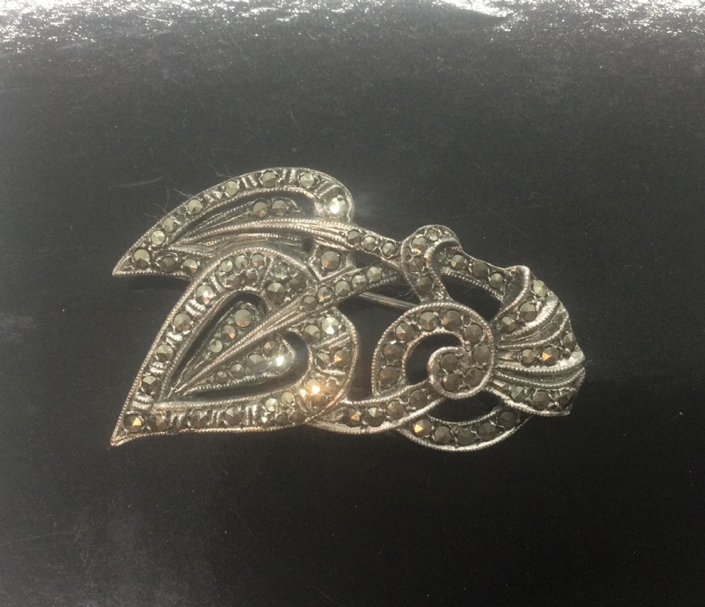 An Art Deco silver marcasite brooch featuring two stylised overlapping hearts connected with swirling ribbon motifs.
