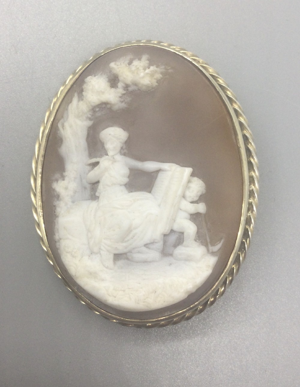 An oval Edwardian cameo brooch depicting a white carved relief scene of classical figures set in a twisted silver frame.
