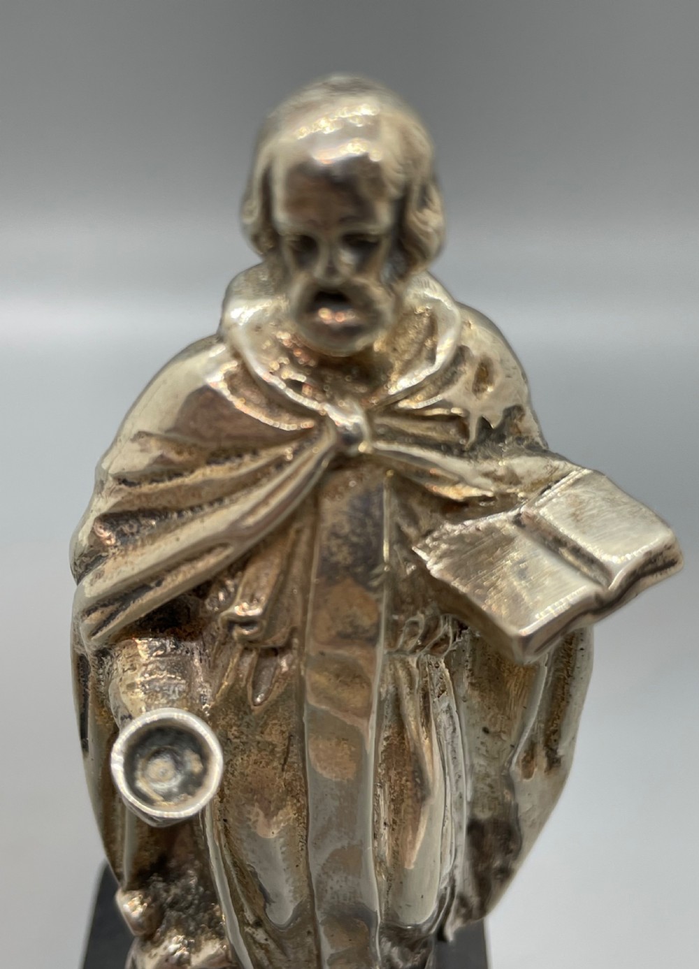 An Edwardian sterling silver figure of an apostle holding a chalice and open book, mounted on a dark square wooden plinth featuring a silver camel motif. View X