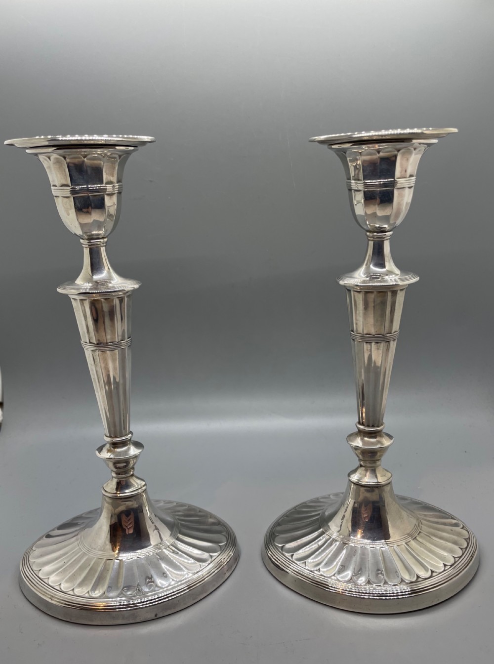 A pair of Victorian sterling silver candlesticks featuring fluted tapered shafts, sconces with reeded rims, and circular lobed bases.