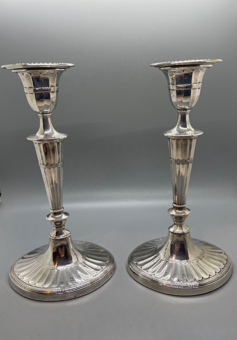 A pair of Victorian sterling silver candlesticks featuring fluted tapered shafts, sconces with reeded rims, and circular lobed bases. View XV