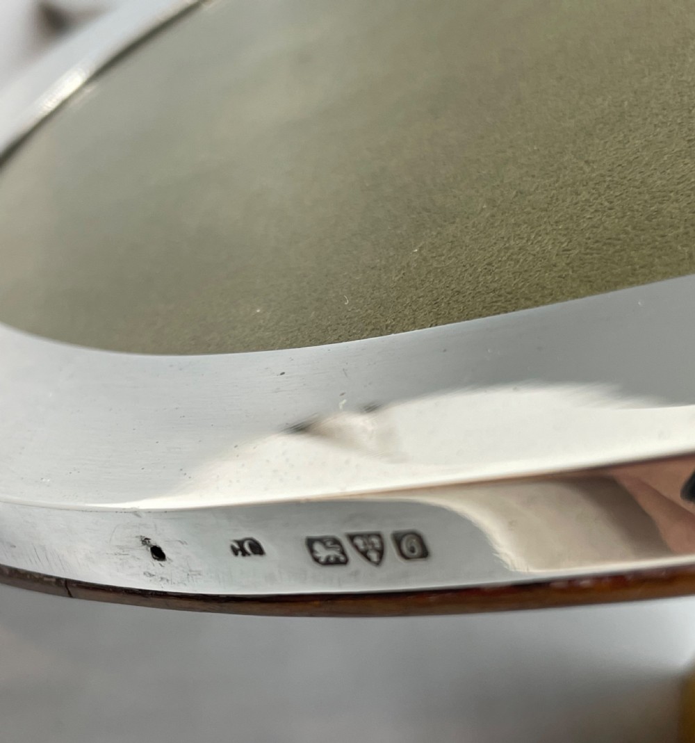 An oval sterling silver photo frame featuring two outward-curving bracket feet and a wooden easel back support. View VII