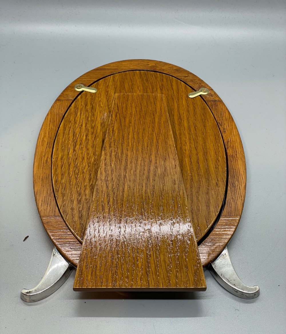 An oval sterling silver photo frame featuring two outward-curving bracket feet and a wooden easel back support. View VIII